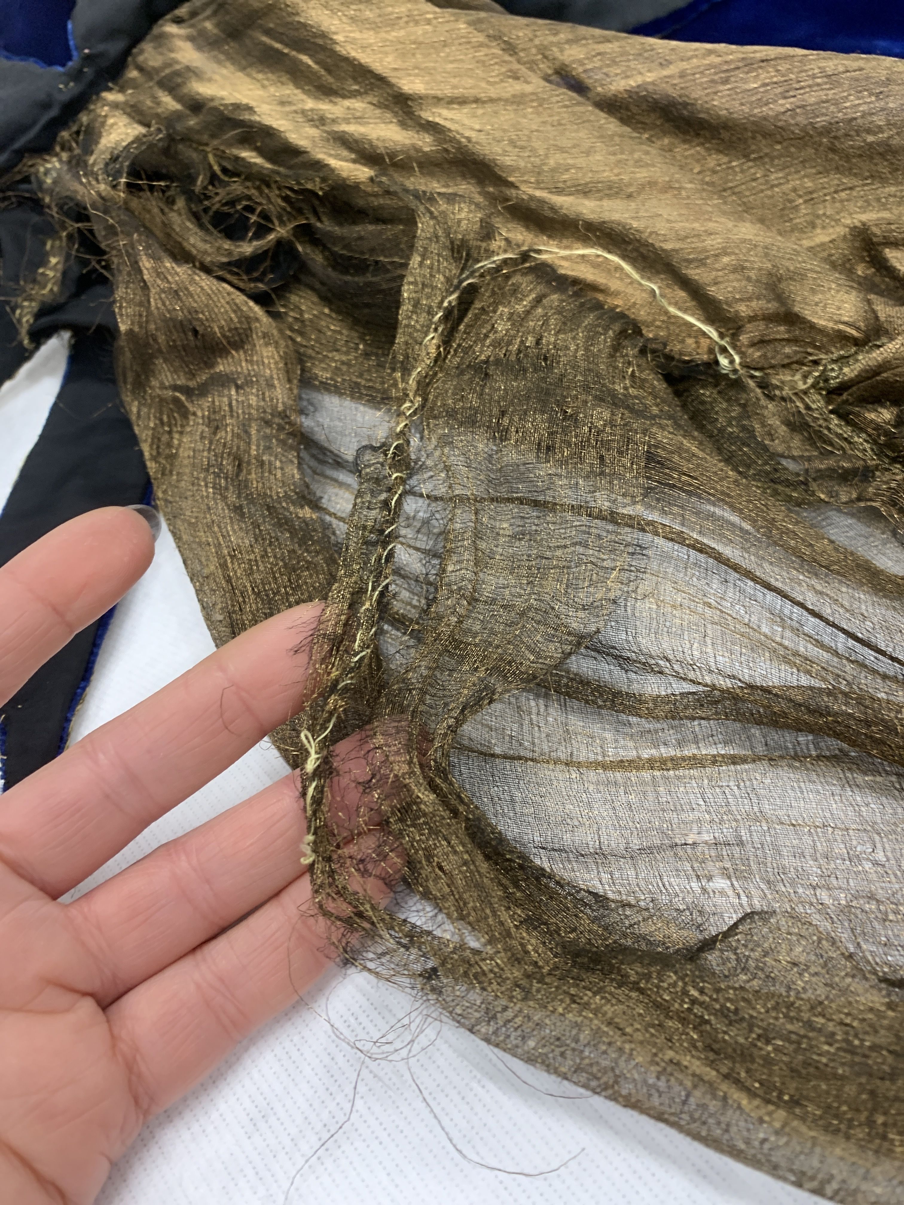 A hand supports part of a piece of golden fabric, showing tears and holes in the material