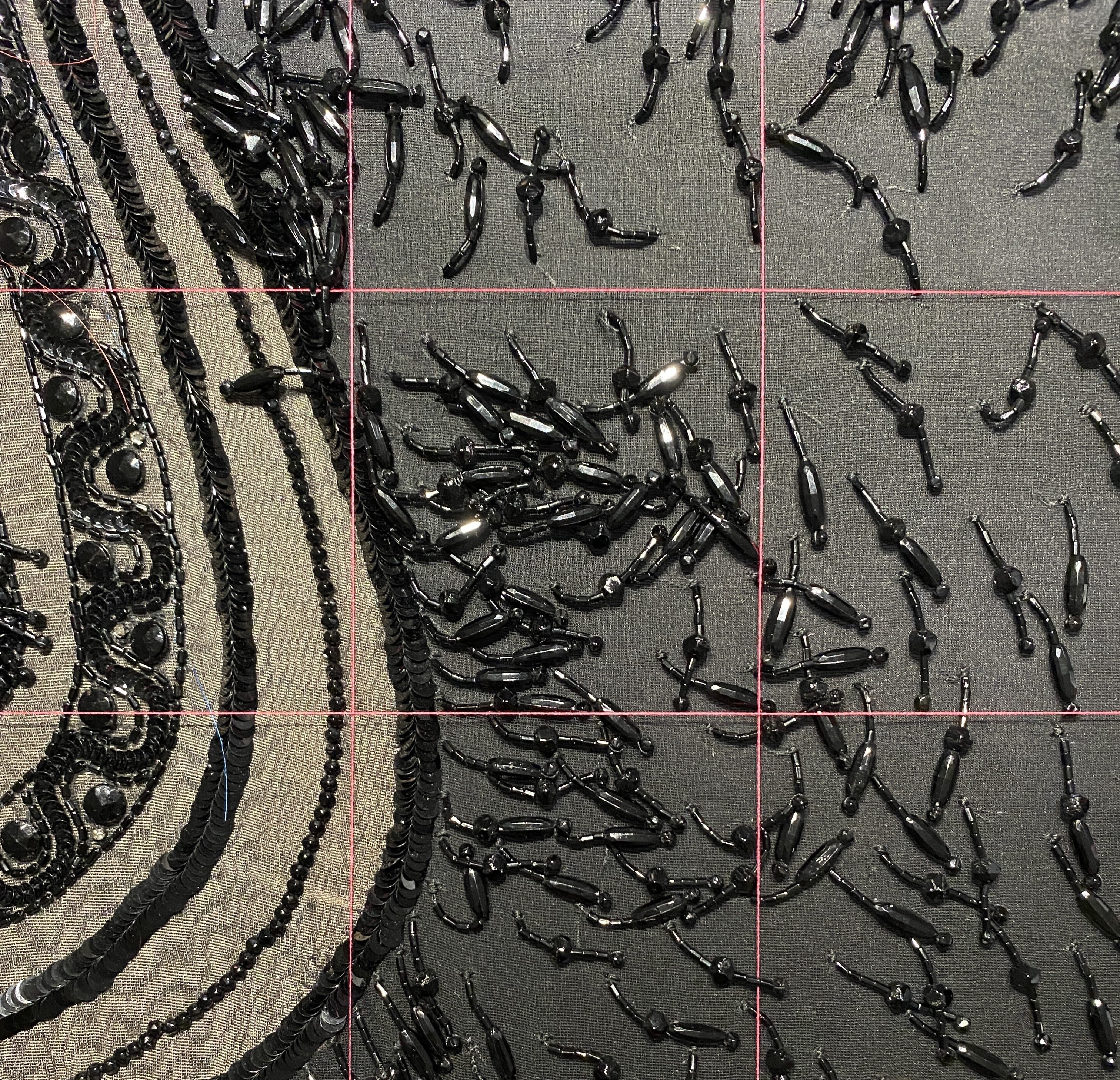 A close-up of the black glass beads against dark fabric, with a red thread grid placed over the material