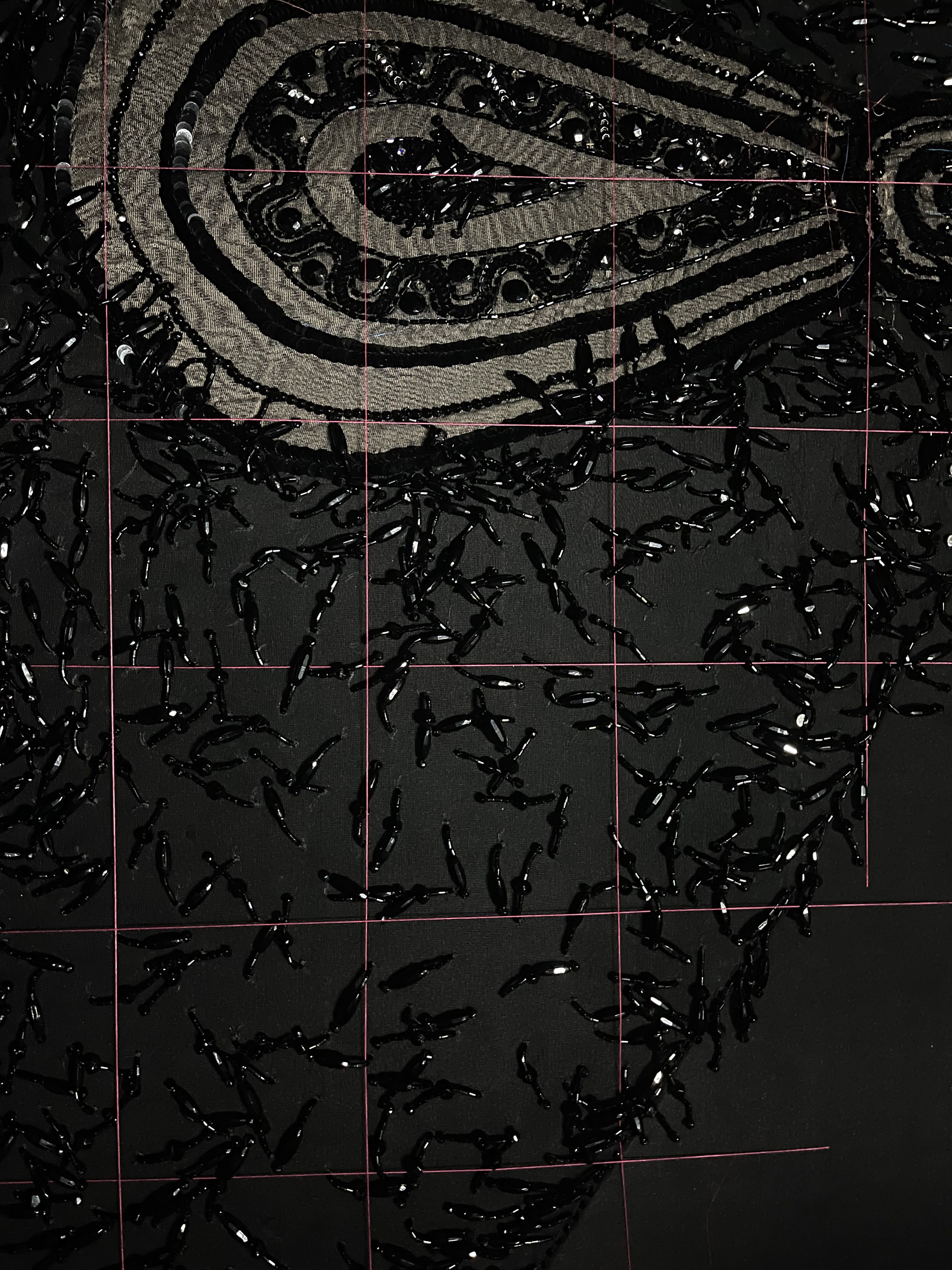 An area of dark fabric from the costume, with dark glass beads on it, overlaid with a grid of red threads
