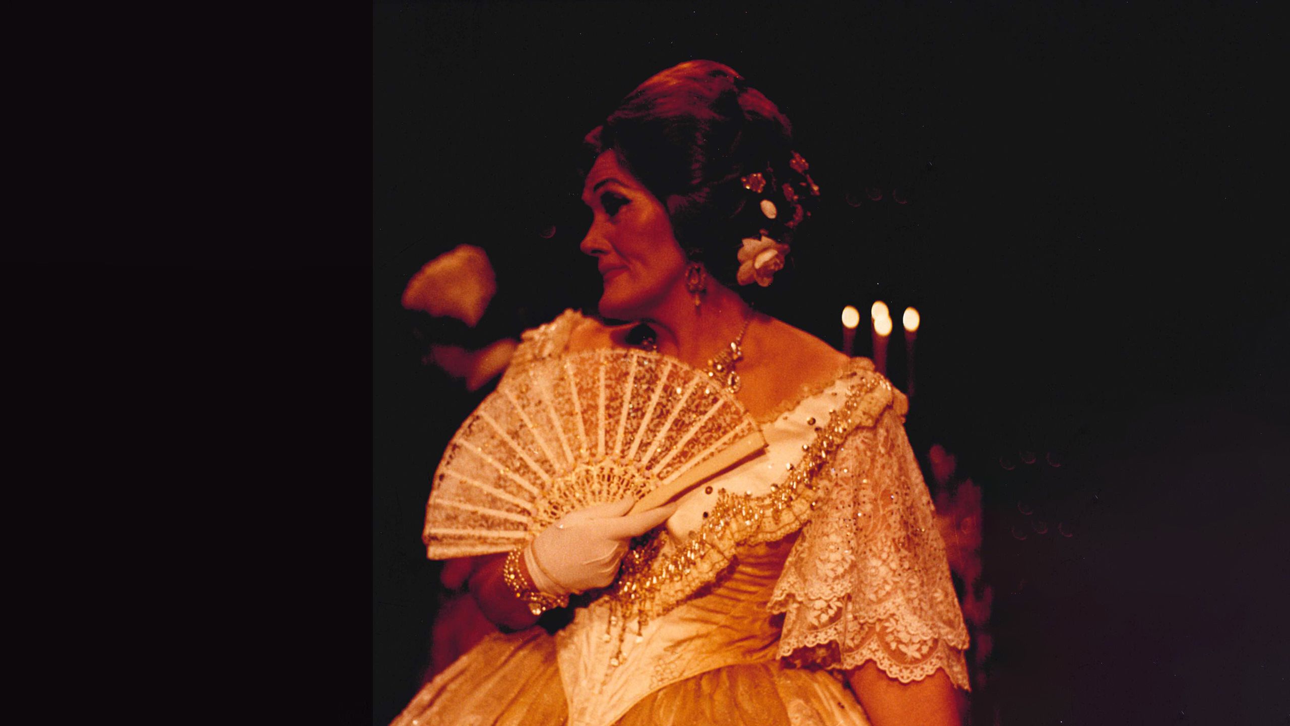 An informal photograph of Joan Sutherland holding a fan and looking to the side while wearing the dress seen in the previous image