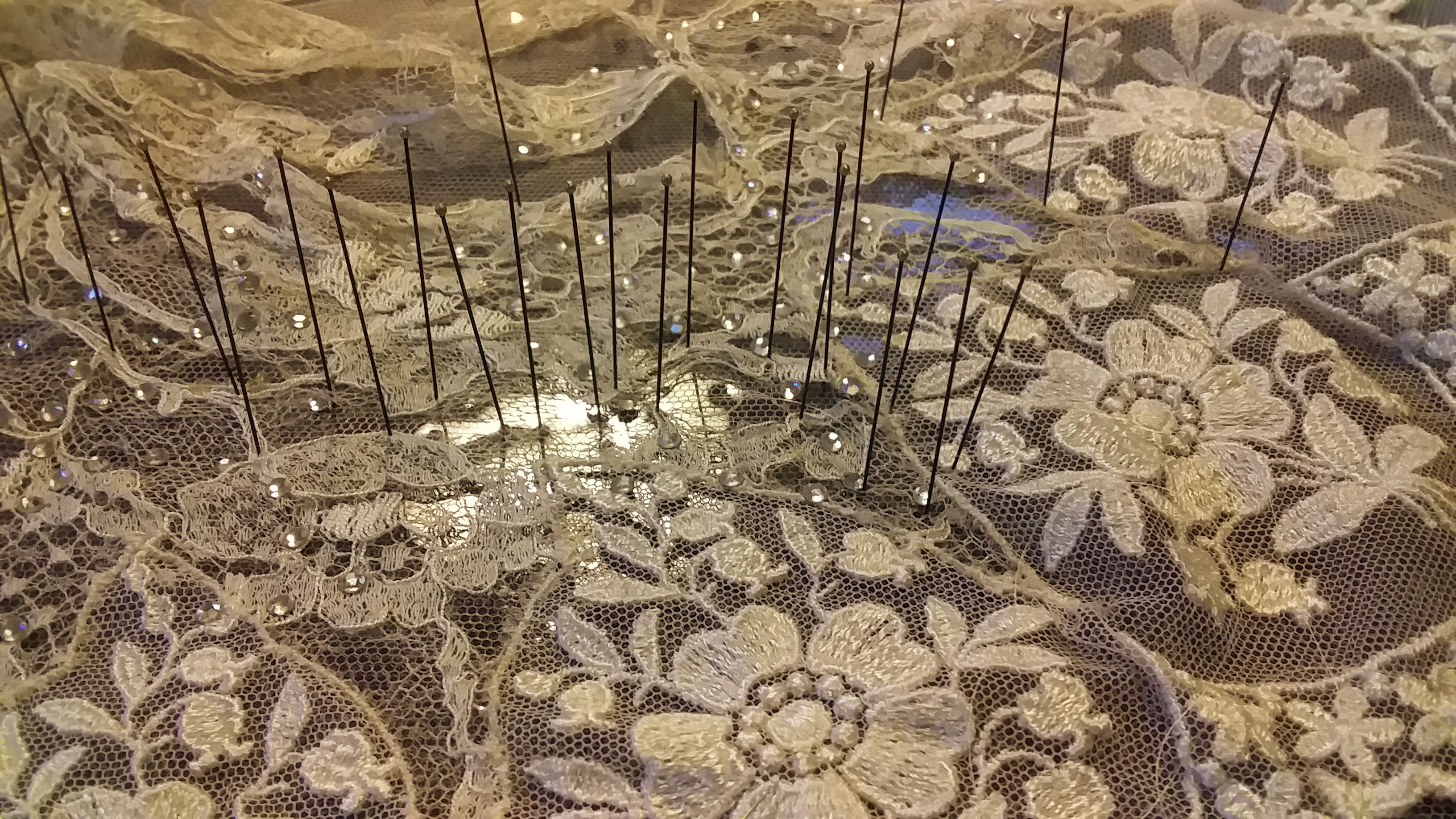 A piece of lace, pinned to a dark background with long pins