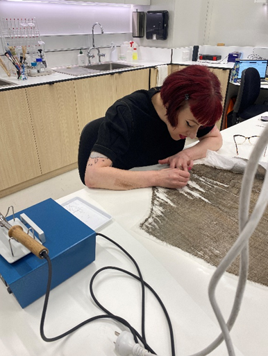 A conservator works at a table in the conservation lab, piecing together tears in the golden fabric