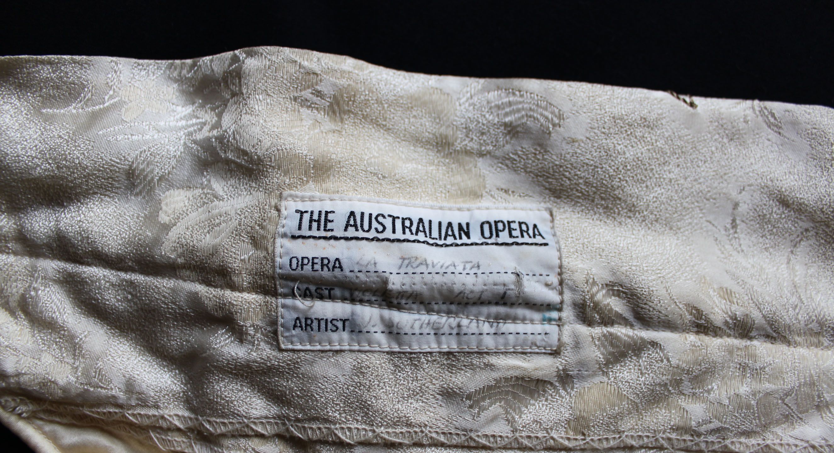 A close up of a label sewn into the neck of a costume, reading, "The Australian Opera. Opera: La Traviata, Cast: Violetta Act I, Artist: J. Sutherland