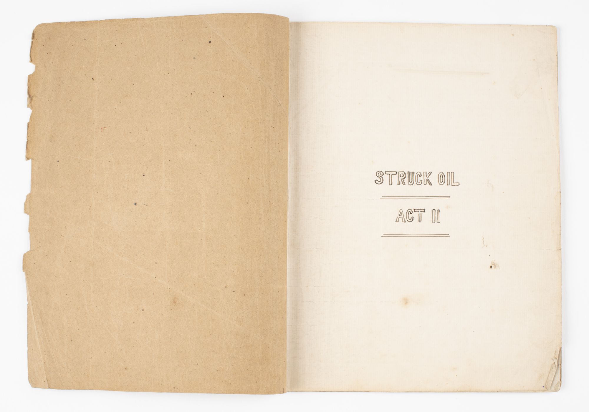 First page of script open. Title 'Struck Oil / Act II' handwritten in block letters on right page. 