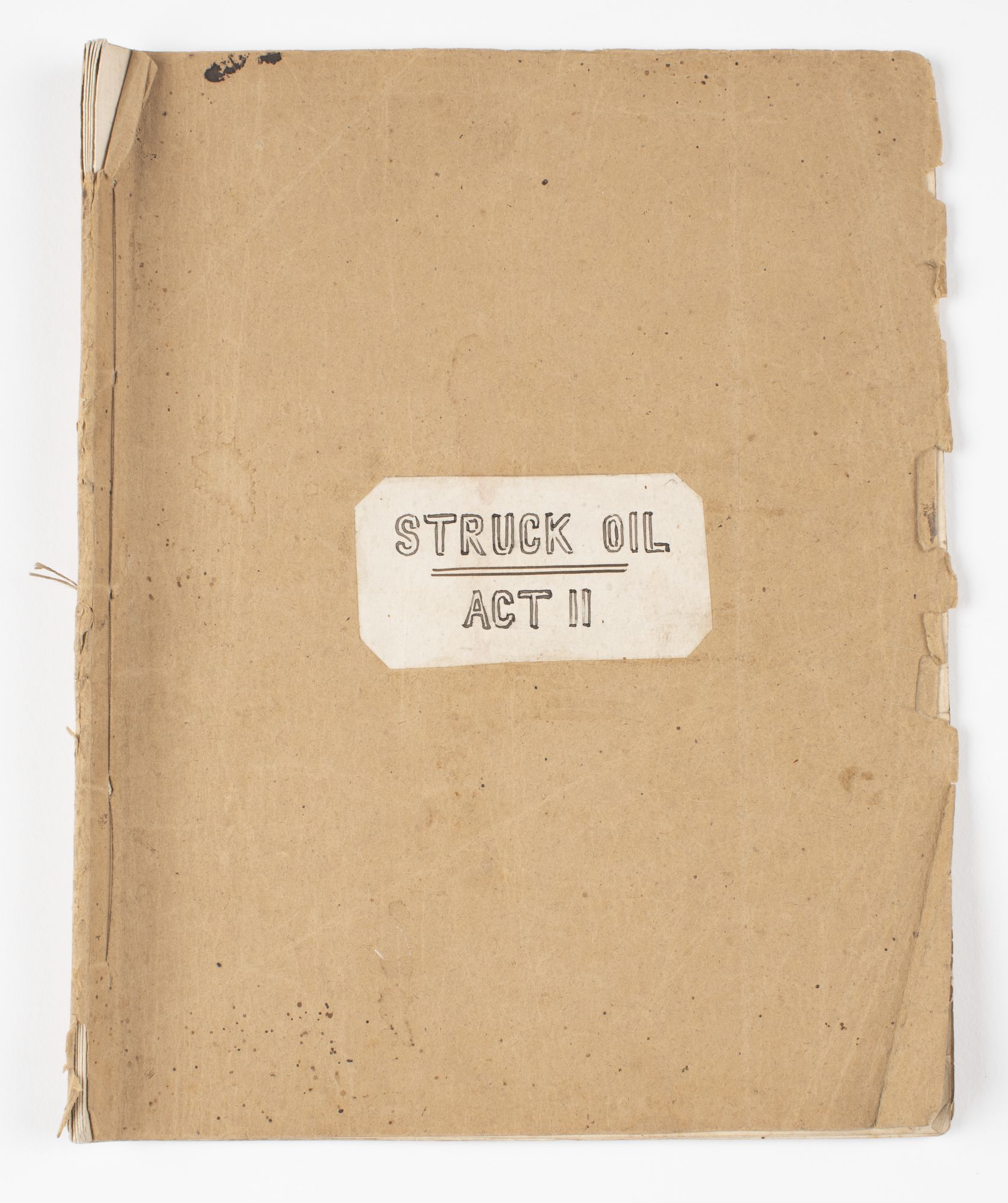 Front page of script bound with string and titled 'Struck Oil / Act II' in handwritten block letters on white stick in centre of front cover. 