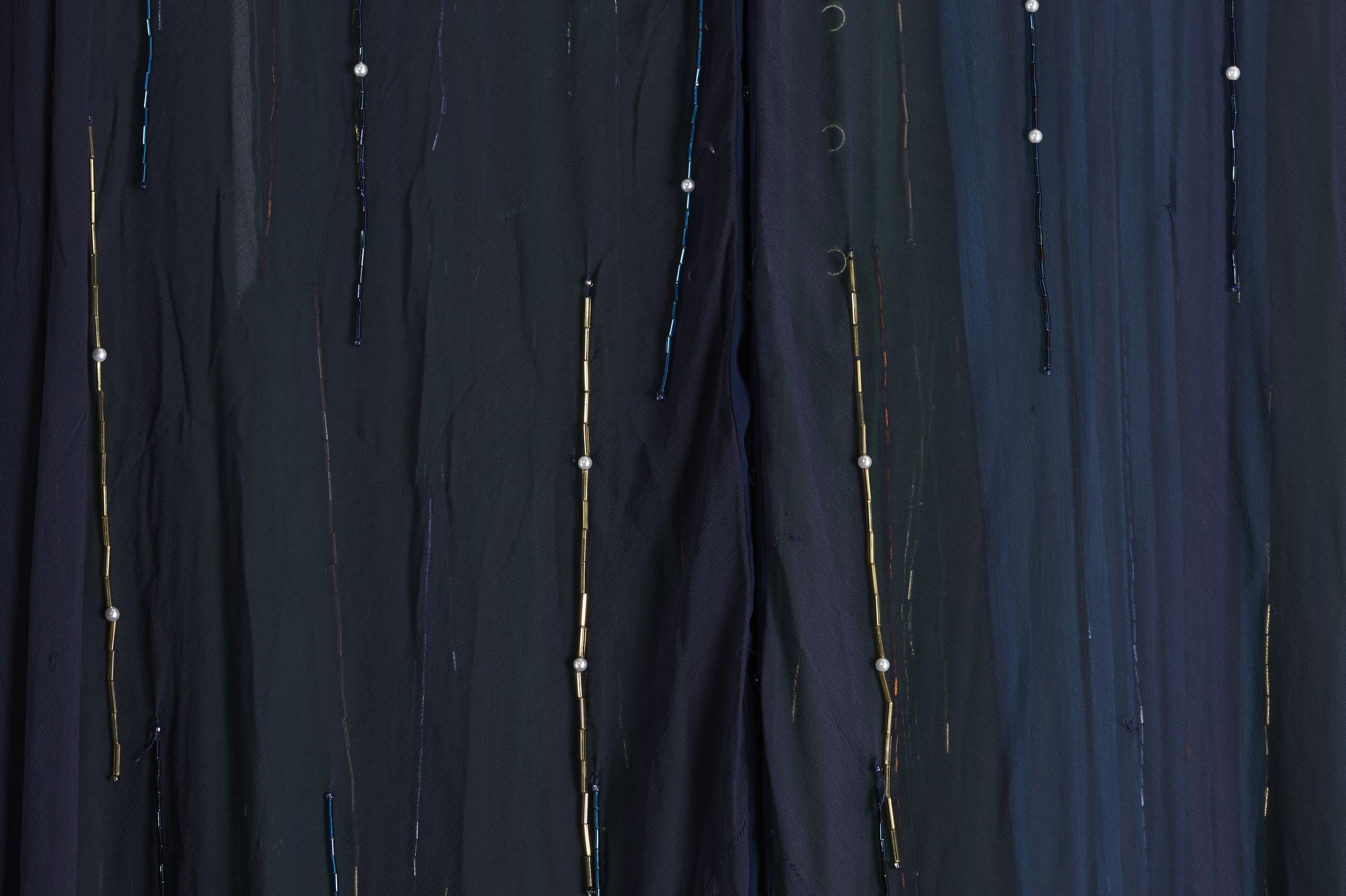 Detail of dress with vertical beading on blue fabric.