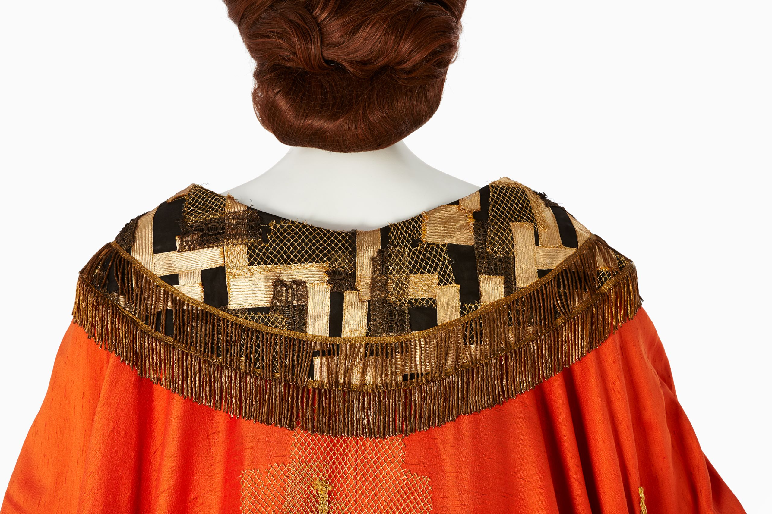 Back view of costume worn by Joan Sutherland for the title role of Semiramide, 1965. The costume is made from heavy orange fabric, with gold detailing and fringing.