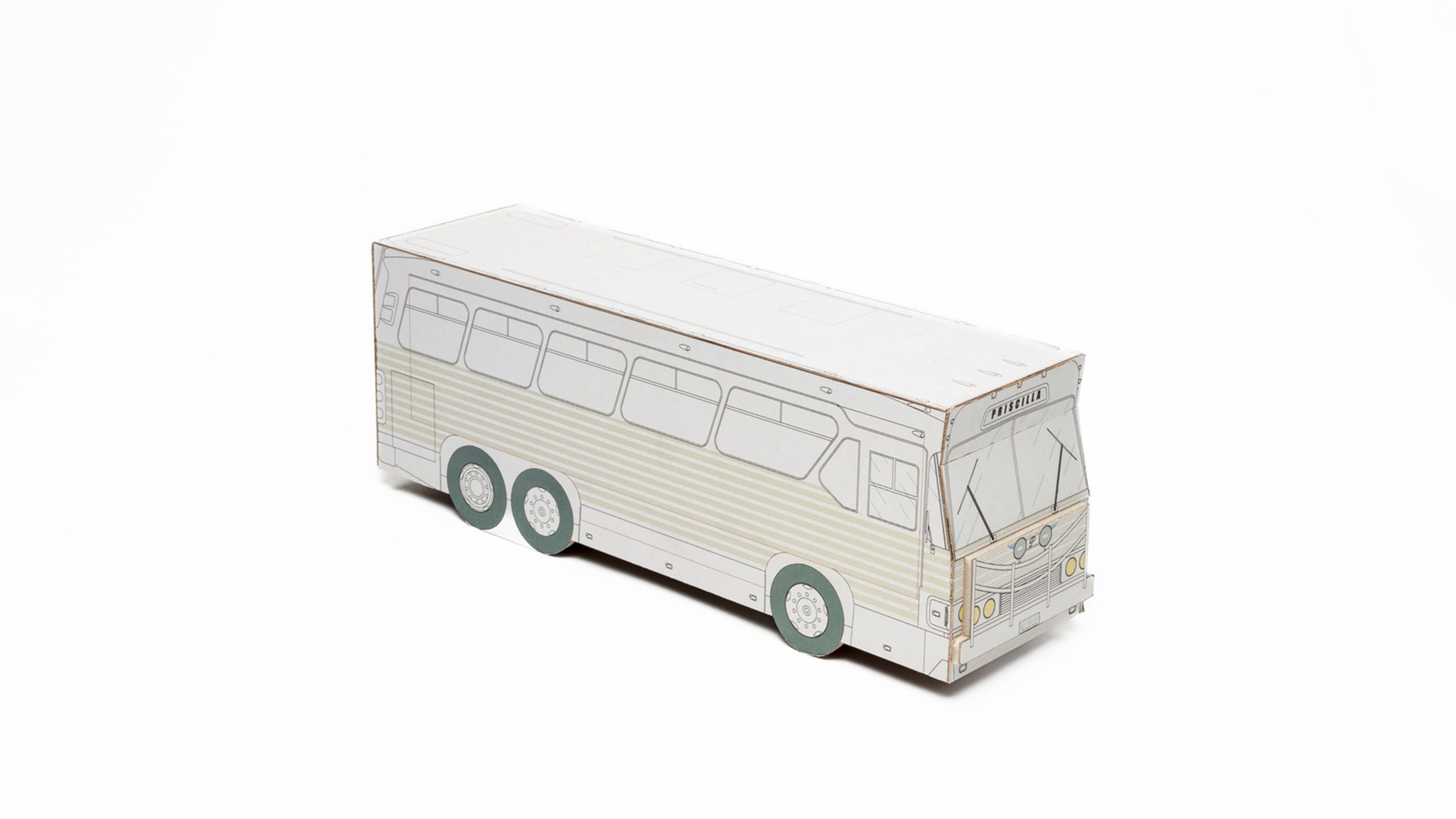 Three quarter side view of 3D bus model made of white cardboard with black lines depicting bus details, pale green striped panelling, grey/green tyres and yellow headlights. The name Priscilla printed in black above windscreen.