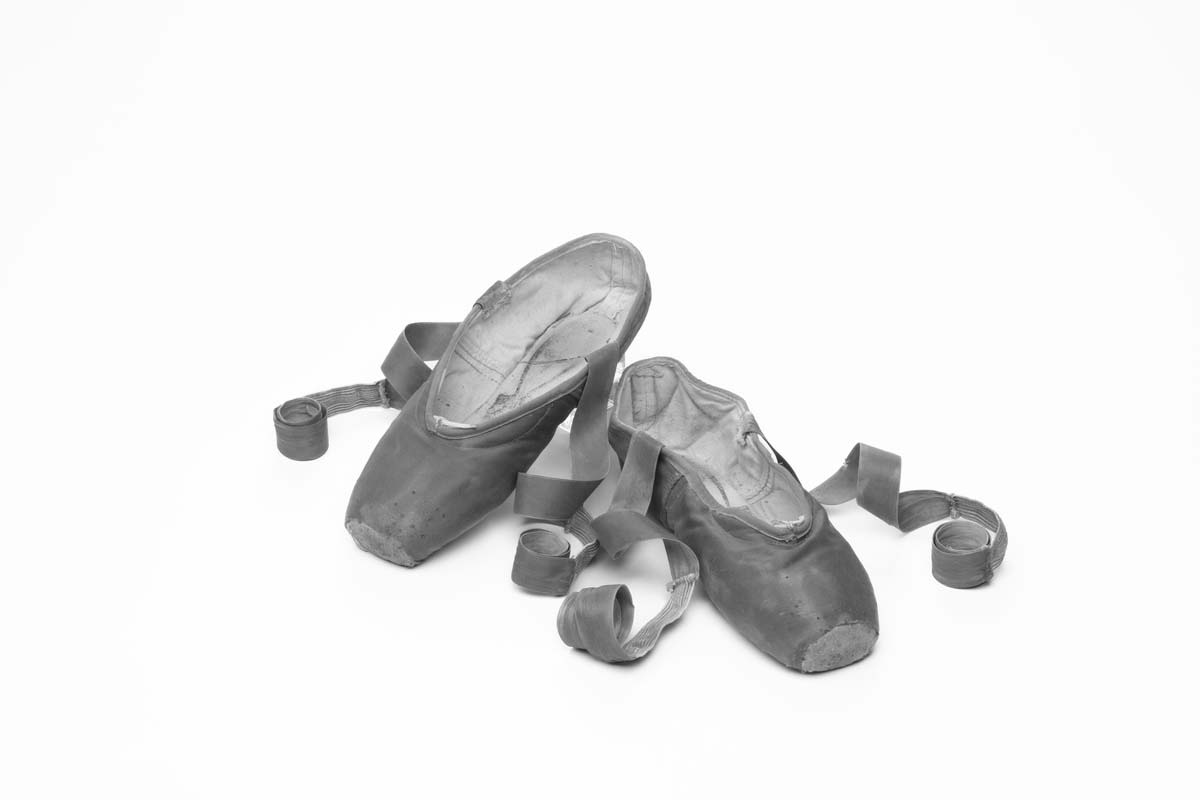 Black and white image of worn ballet shoes with ribbons curled to the side.