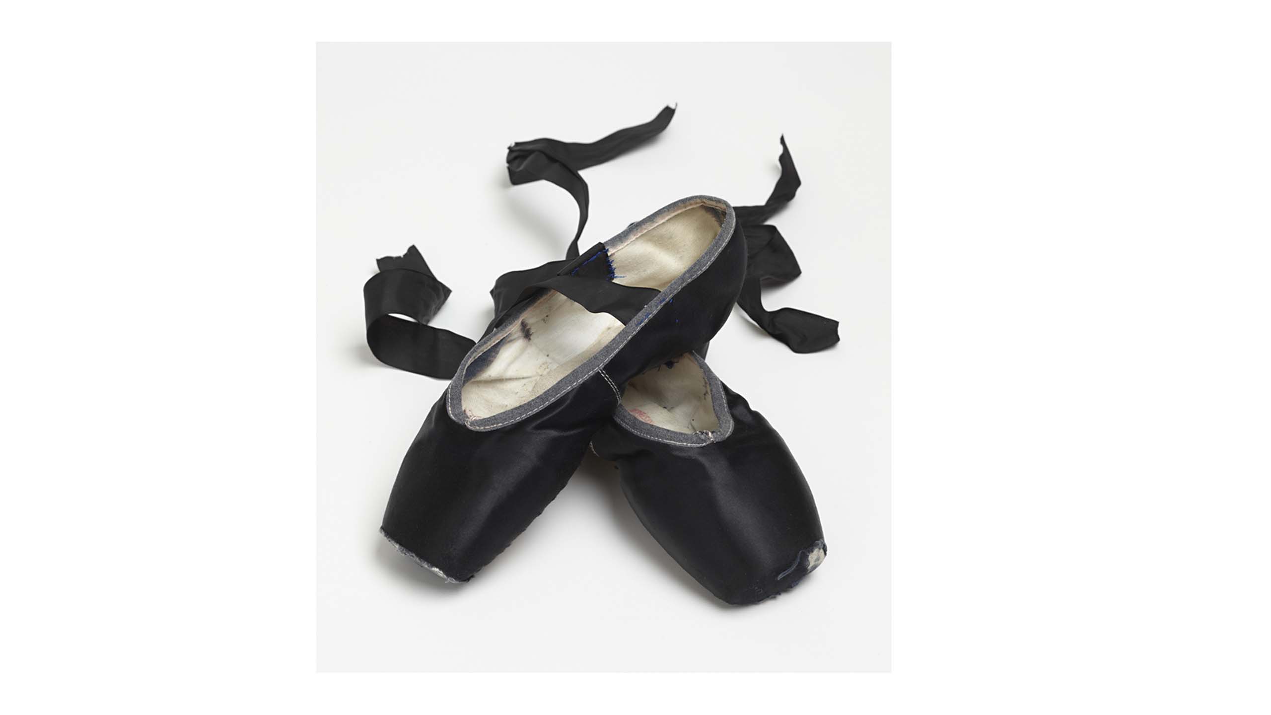 Black ballet shoes with white satin insoles and ribbons curled to the back.