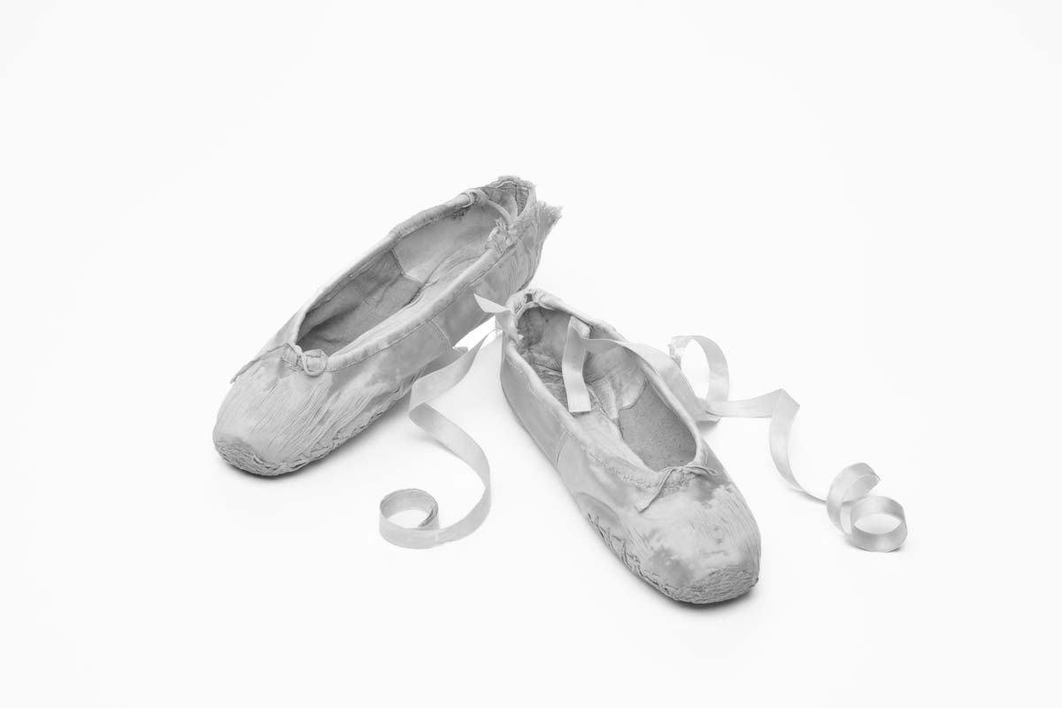 Black and white image of ballet shoes with ribbons curled to sides and with darning on toe..