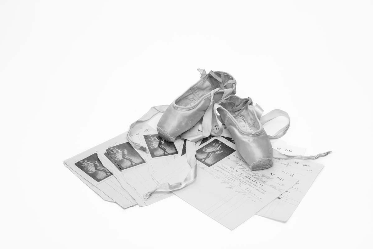 Black and white image of ballet shoes resting on fanned our pieces of paper.