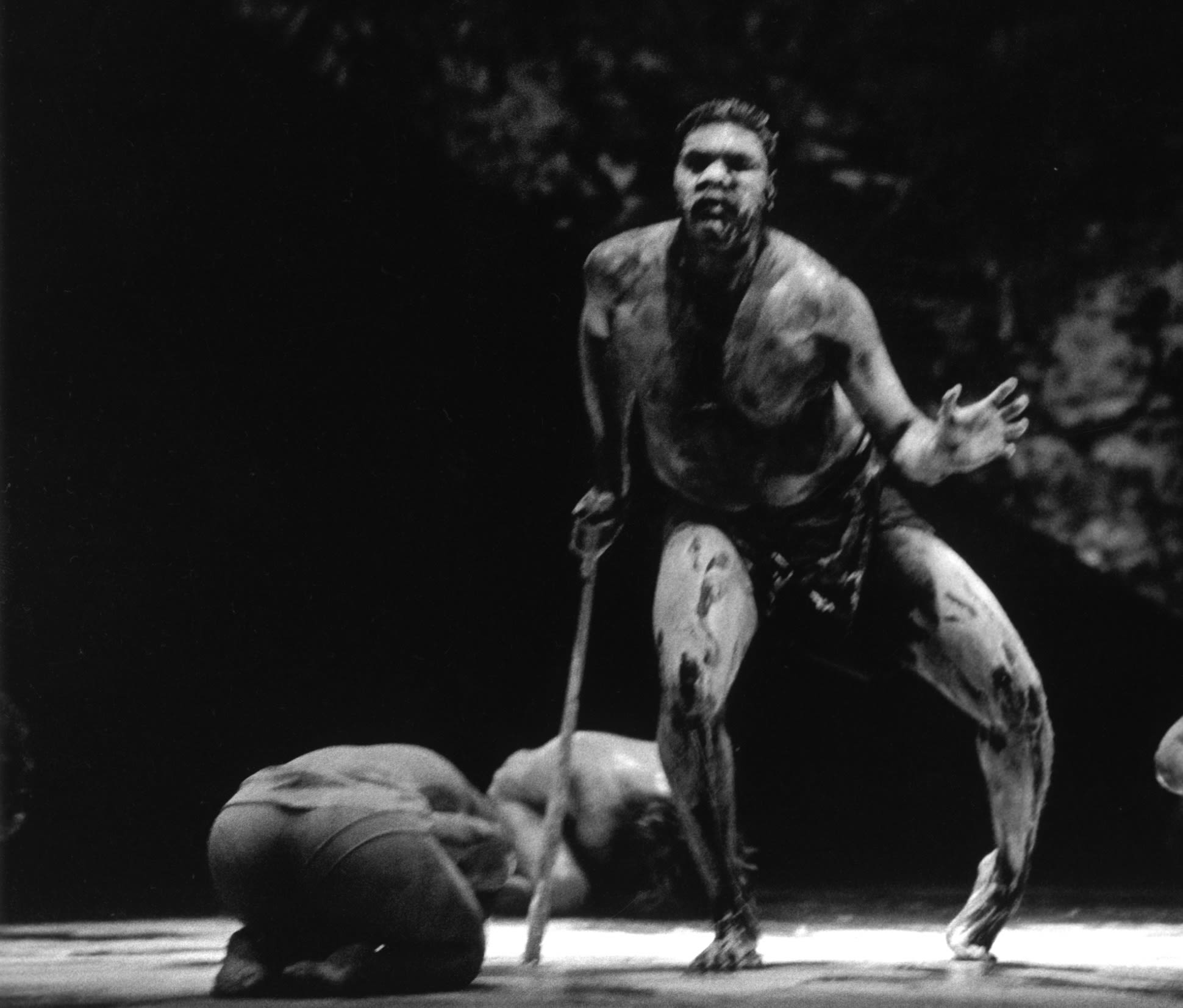 Bare-chested male dancer on stage leans on a walking stick.