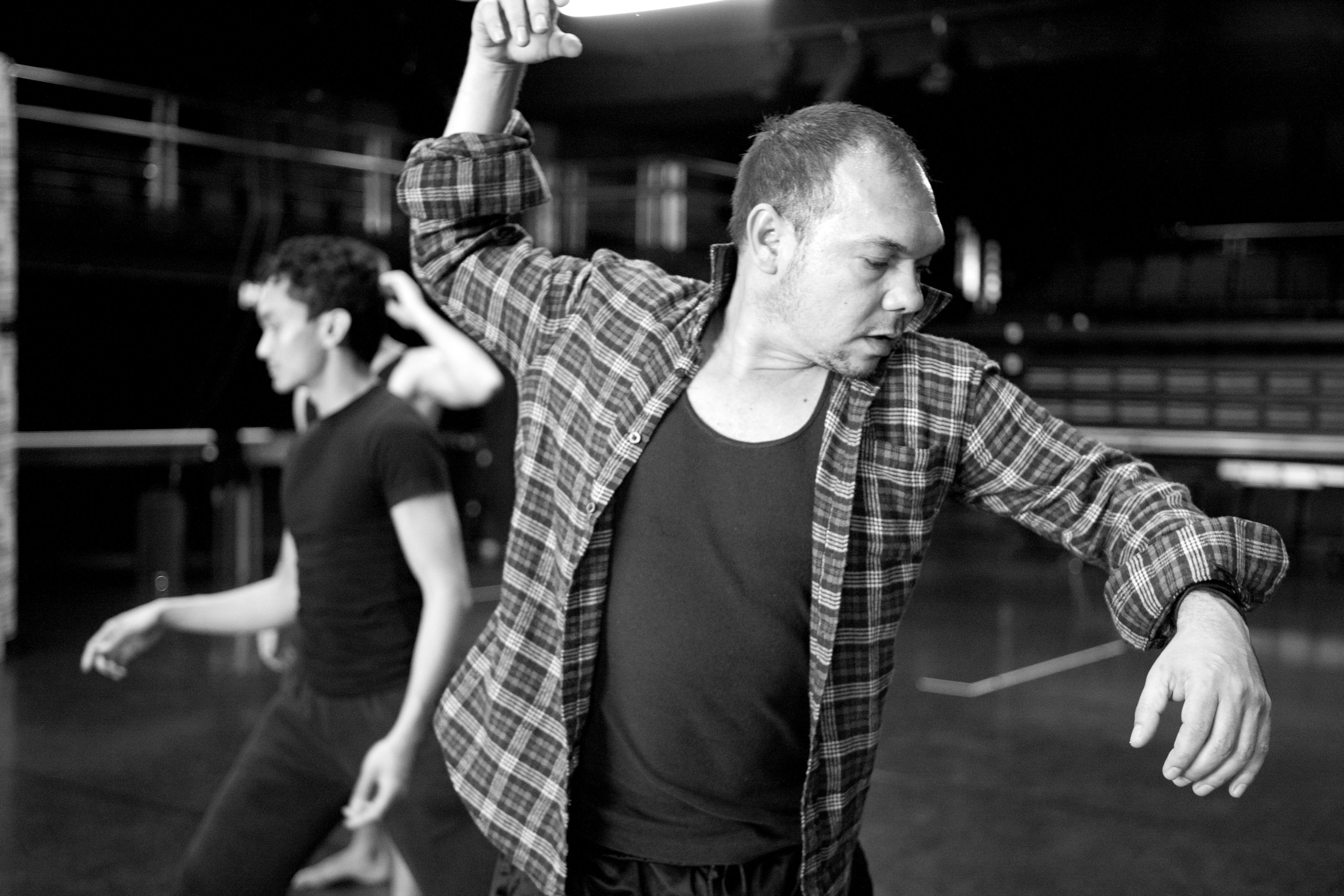 Black and white photo of man in dance studio looking sideward and down.