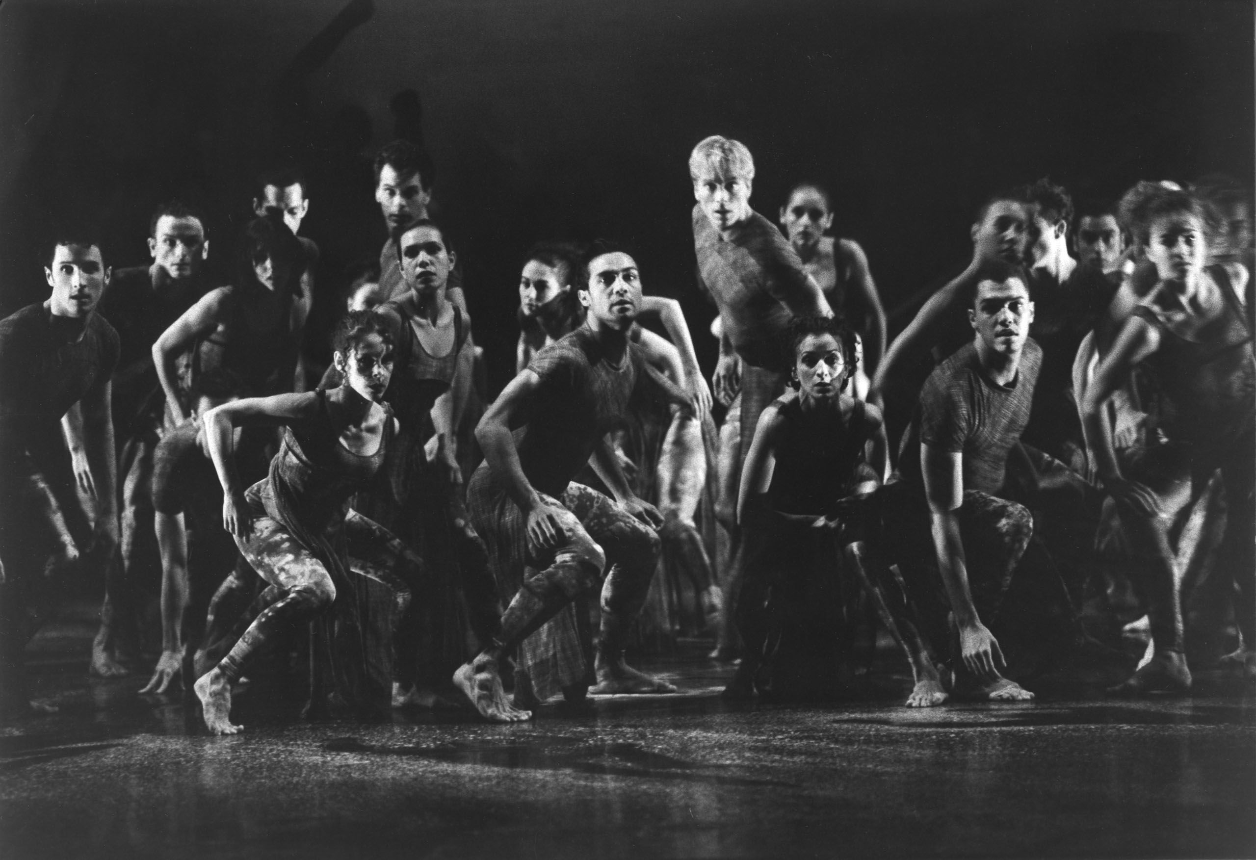 Large group of dancers gathered in the centre of a stage, looking forward.