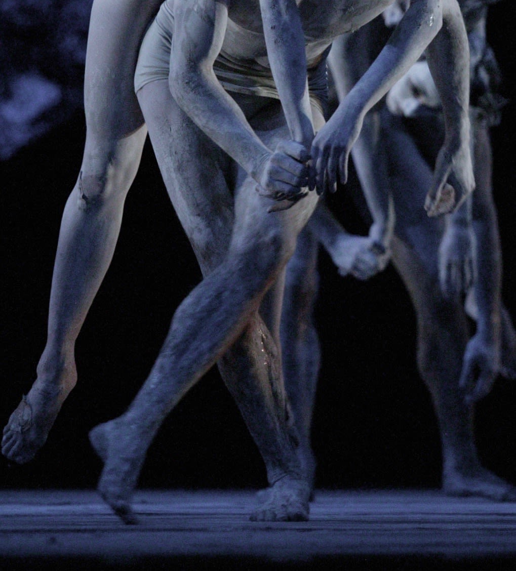 Close of white-painted, crouching, dancers hands and legs