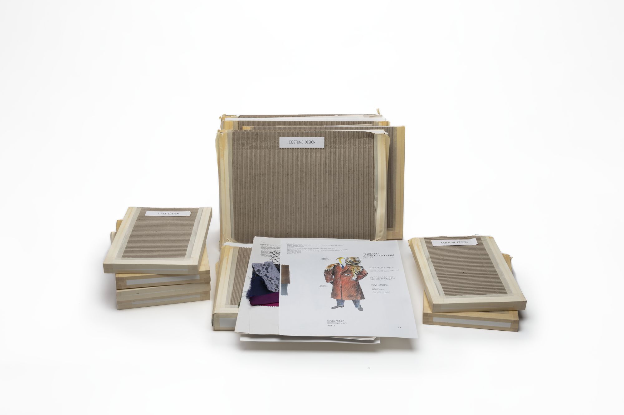 Numerous corrugated cardboard folders with labels. Two hand drawn costume designs feature in the foreground.