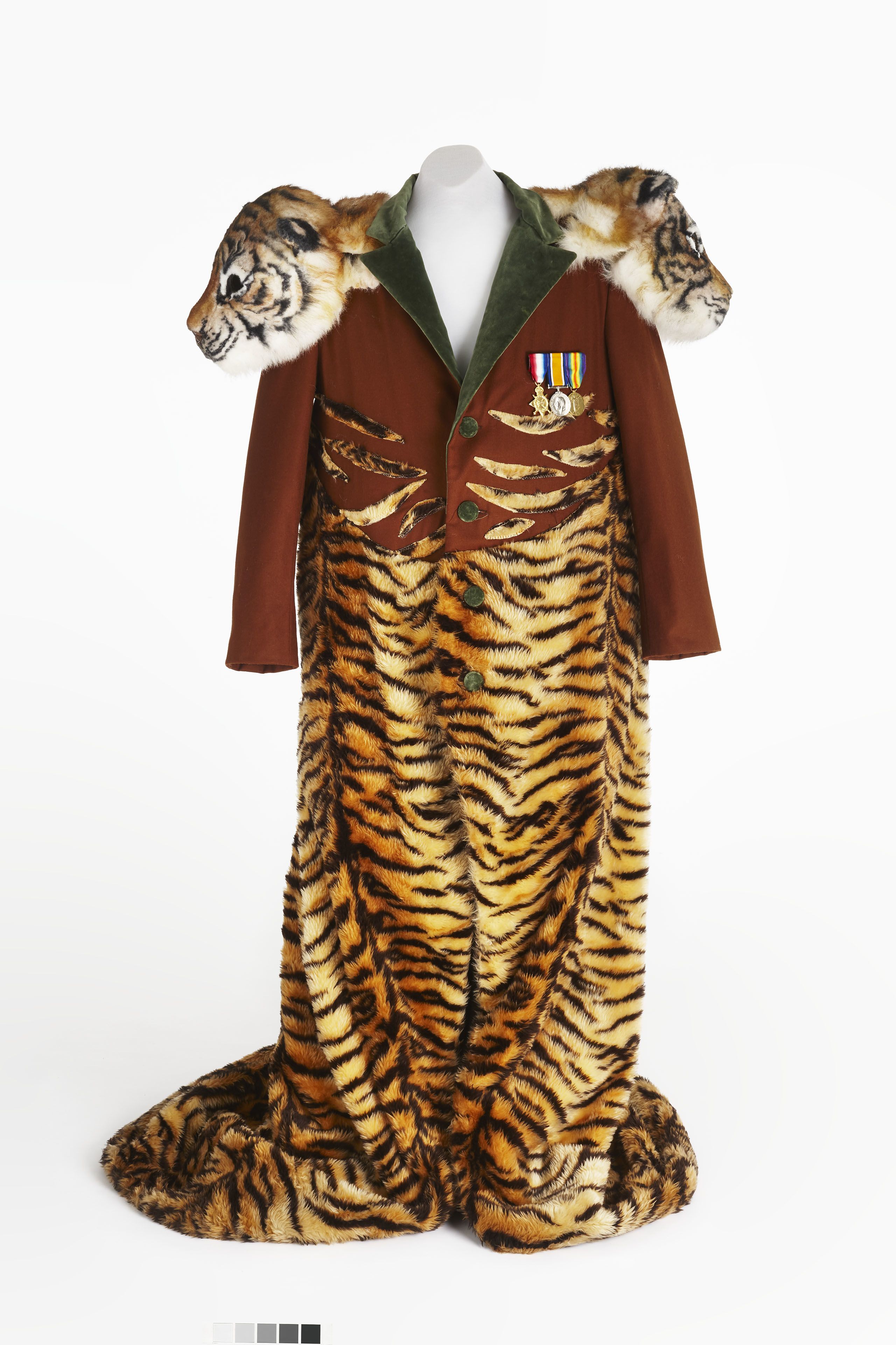 Close up of a man's costume on a white mannequin. It features a brown coat, with green lapel and buttons, three medals and tiger stripes. Each shoulder features a 3D prop tigers head.