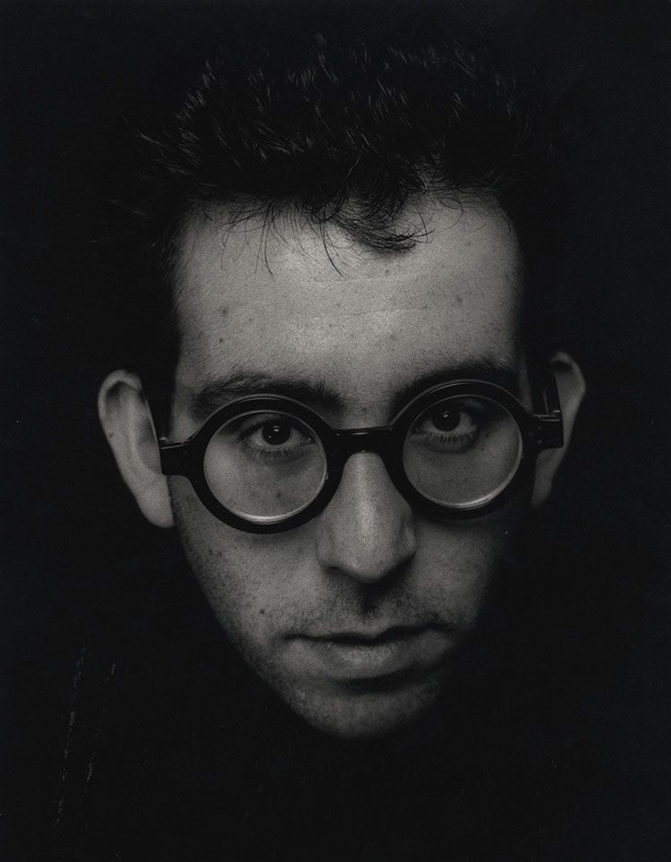 Black and white portrait of male wearing thick rimmed black spectacles.