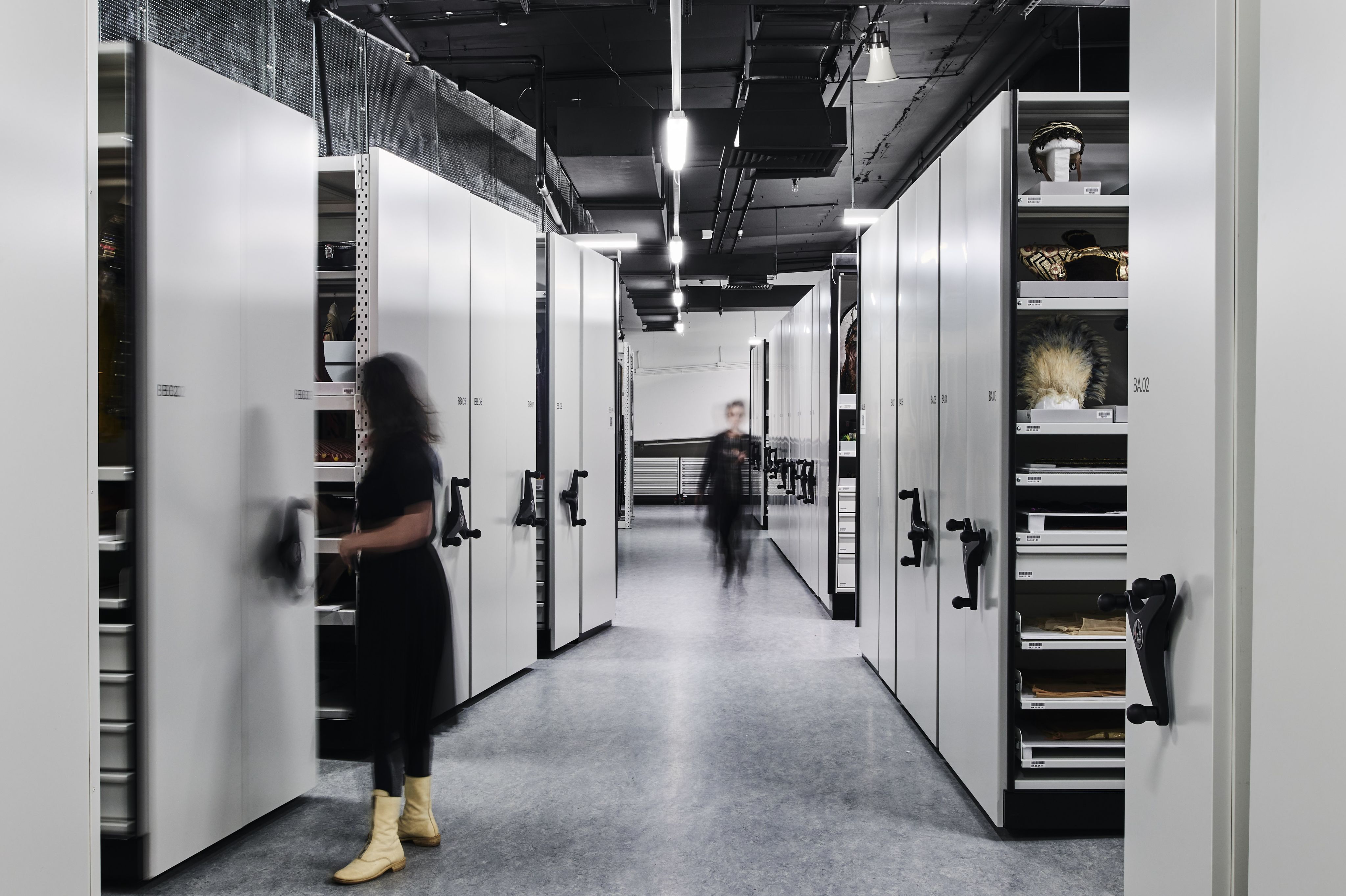 Photograph of a storage facility, with compactus on the right and left sides. Two figures move in the space.