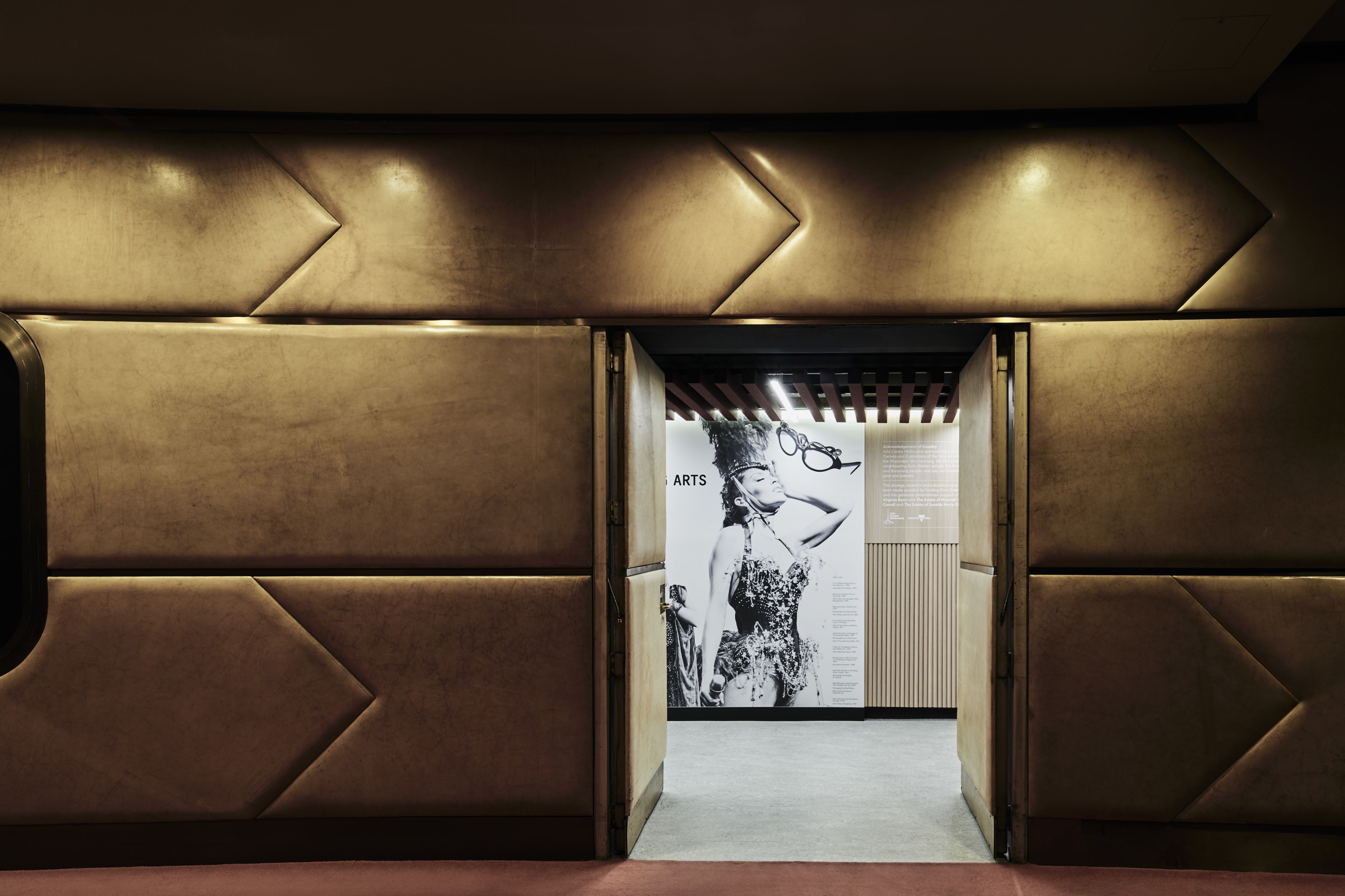Photograph of a leather bound wall, with two open doors leading do a walkway with black and white photography wallpaper.