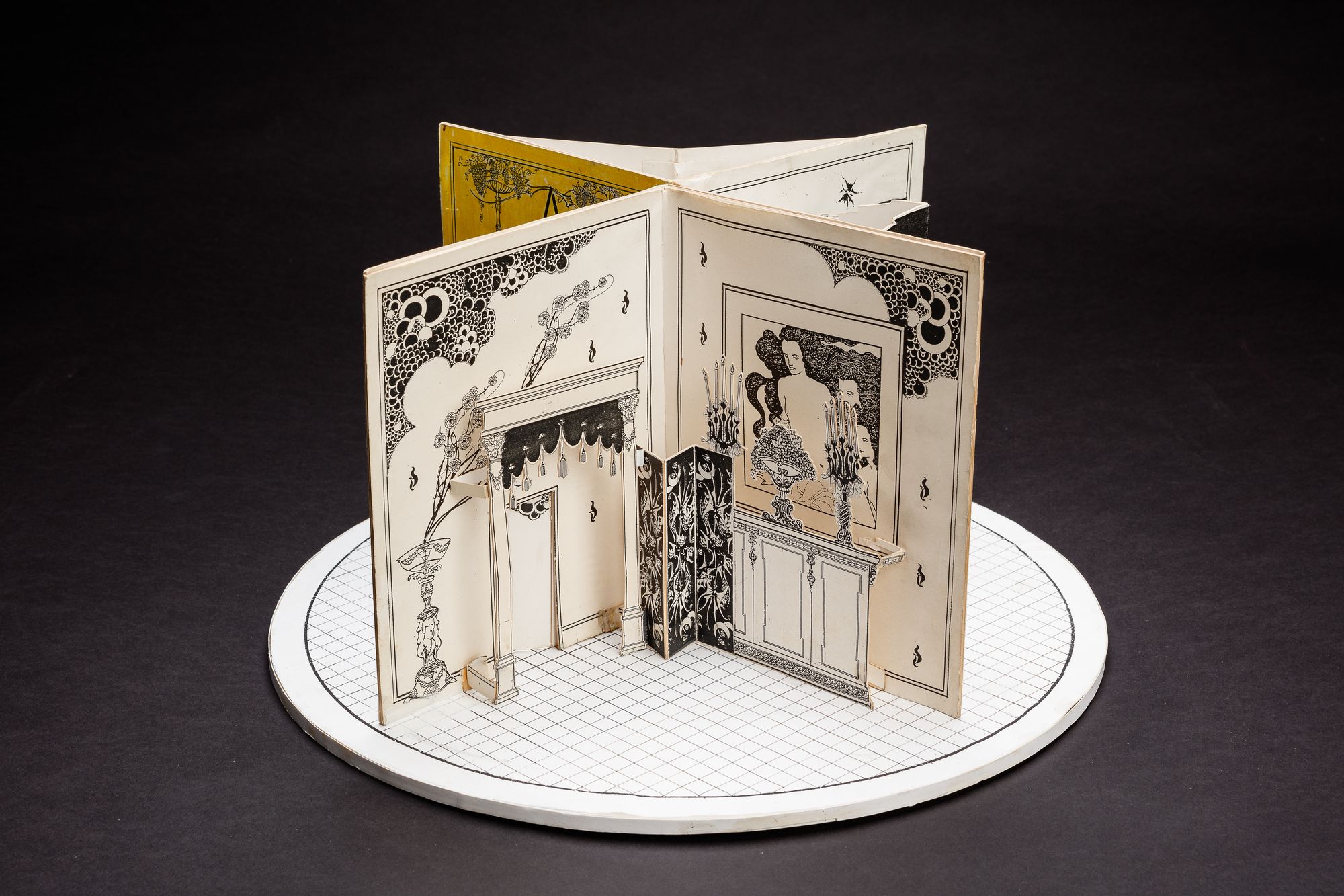 A cardboard set model on a circular stage, designed to resemble a large open book.