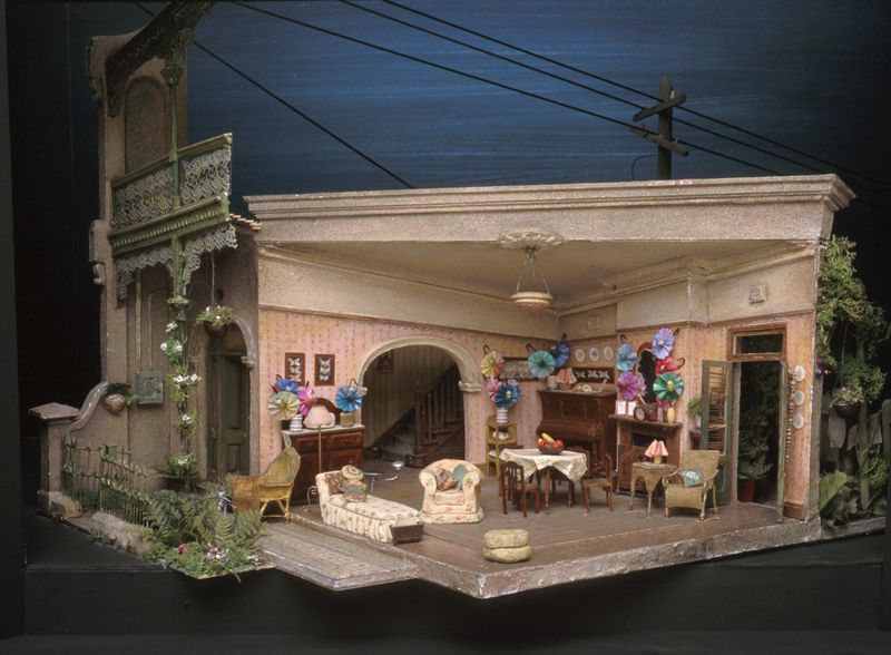A large set model showing the detailed 1950s-style interior of a Victorian terrace house, dotted with dolls.