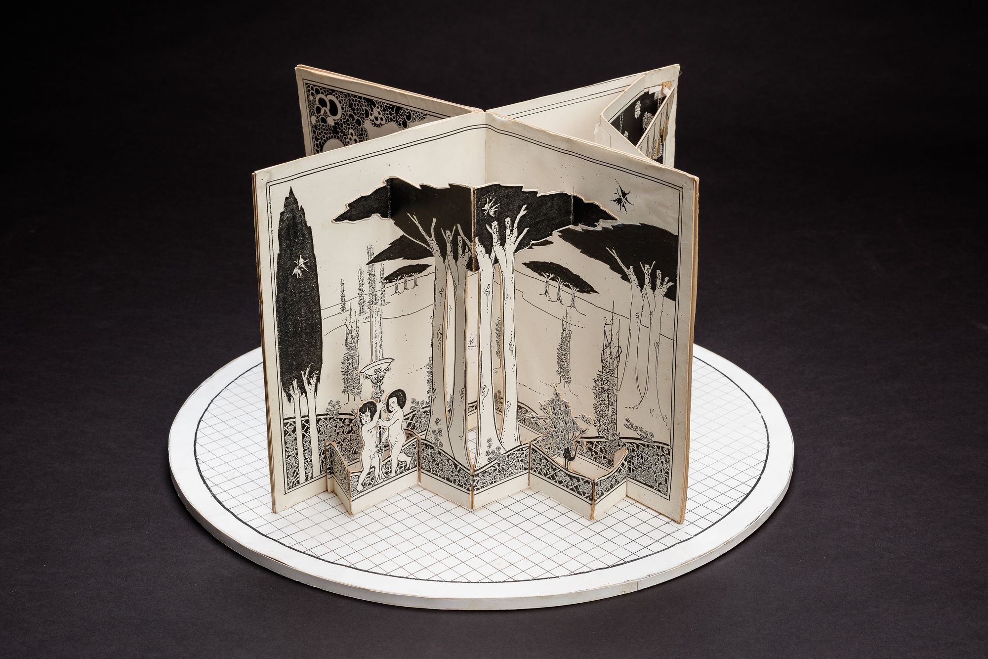 A cardboard set model on a circular stage, designed to resemble a large open book.