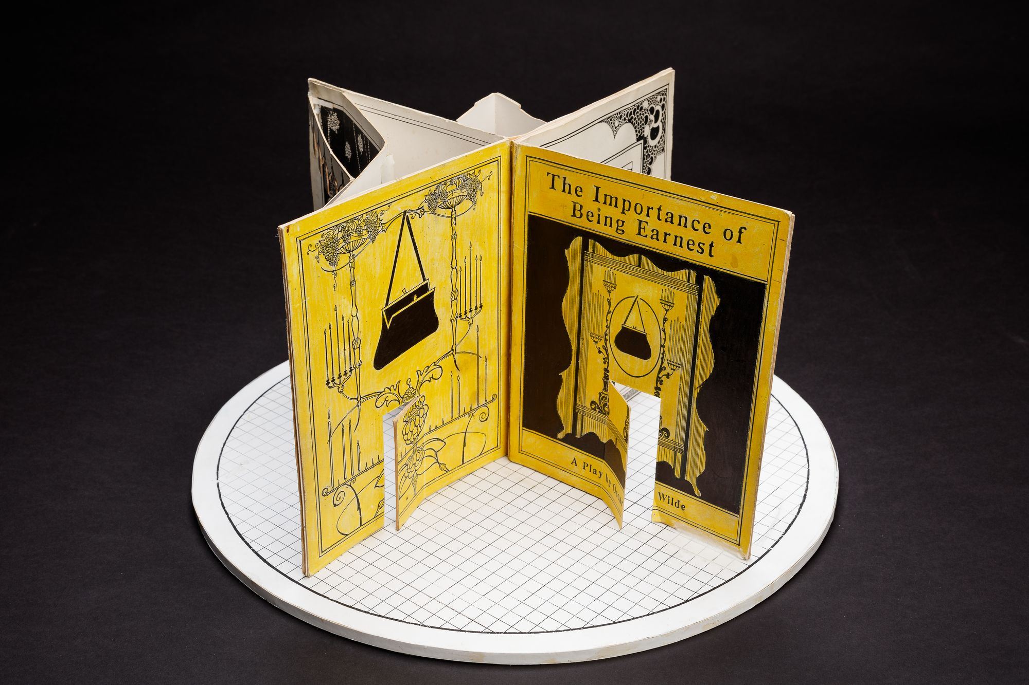A cardboard set model on a circular stage, designed to resemble a large open book.