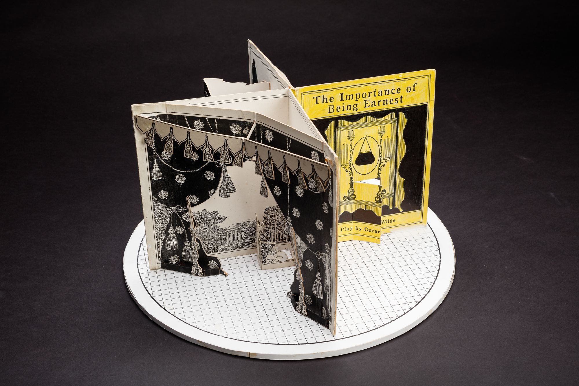 A cardboard set model on a circular stage, designed to resemble a large open book.